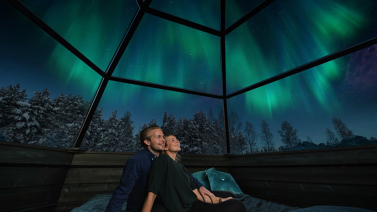 Snow-covered log cabin in Finnish Lapland under the glowing green Northern Lights in December