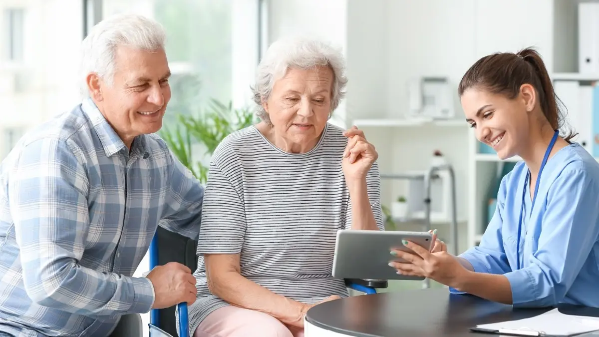 Professional home caregiver offering support to an elderly client in a comfortable living room