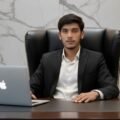 Portrait of Hassan Raza, Content Writer at BrassSmile.media, sitting at a desk in a suit with a laptop.