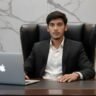Portrait of Hassan Raza, Content Writer at BrassSmile.media, sitting at a desk in a suit with a laptop.