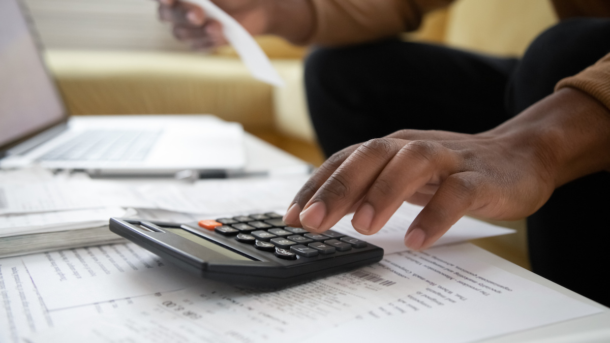 Person at a wooden desk using a calculator with financial documents, reports, and a pen spread out.