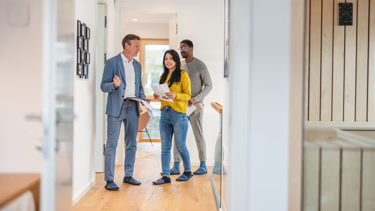 Professional real estate agent in a blazer presenting a house to a couple outdoors, pointing towards the modern residential home.