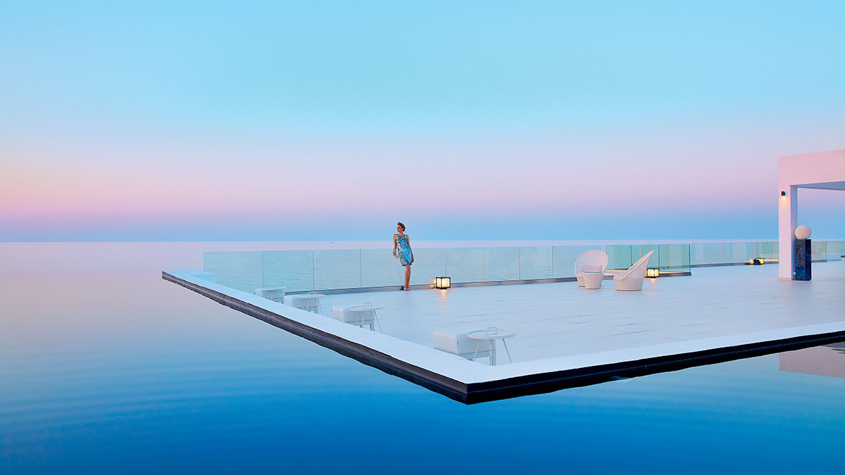 Overwater resort villas extending into a tranquil blue lagoon under a bright sunny sky.