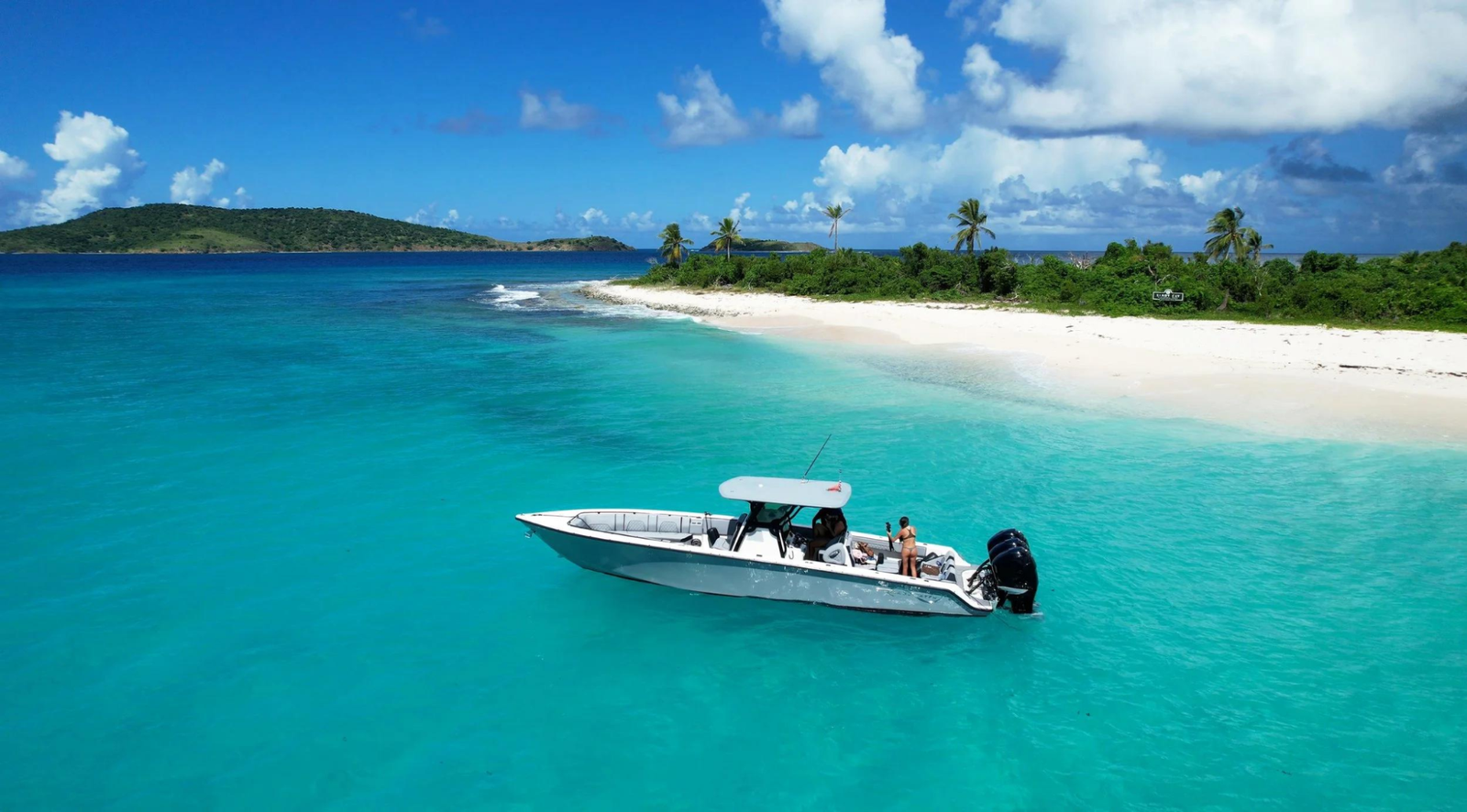 Speedboat cruising through calm turquoise Caribbean water near a secluded white sand beach island shore.