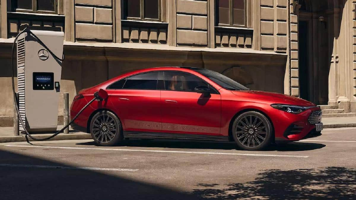 Side view of a red Mercedes-Benz electric sedan parked at a DC fast-charging station with the charging cable connected.