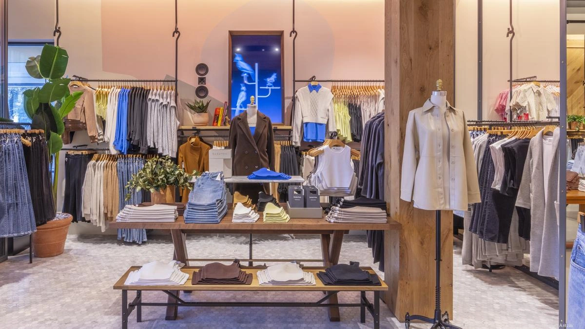 Aritzia boutique interior featuring minimalist wooden accents, warm lighting, and neatly arranged racks of clothing.