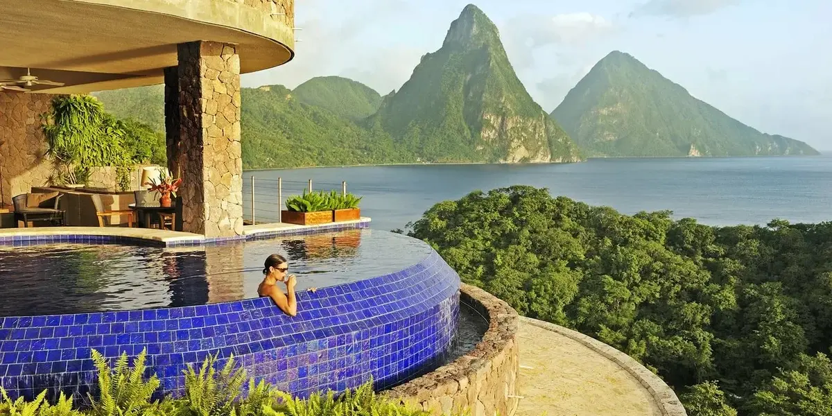 A woman relaxing in an infinity pool overlooking mountain peaks and the ocean at a luxury resort