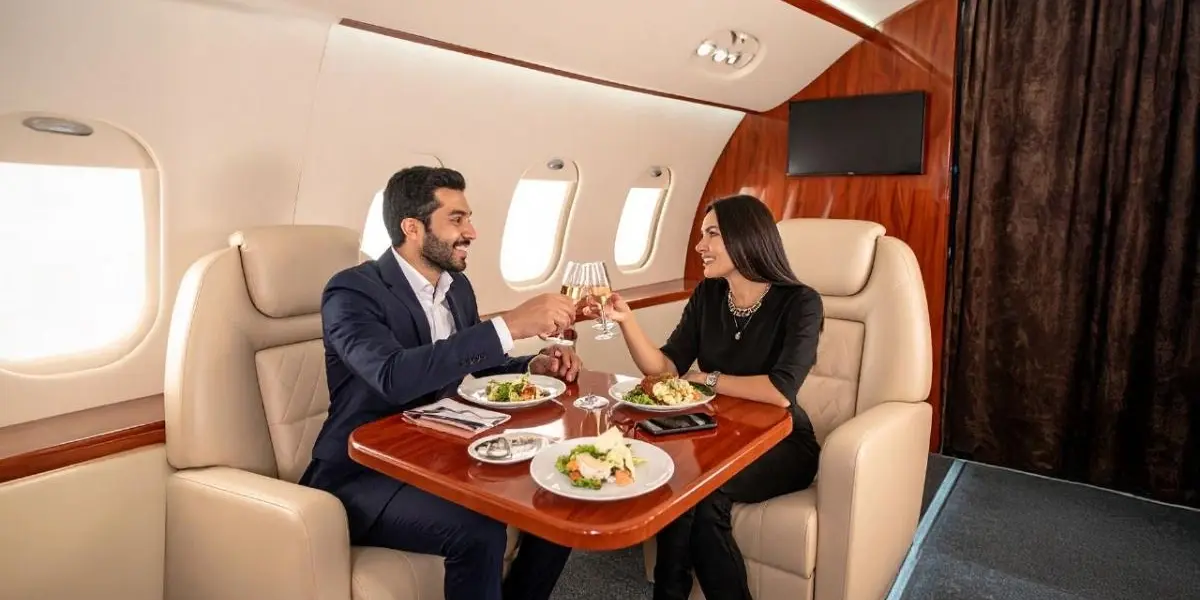 Couple enjoying champagne and a gourmet meal inside a private jet cabin.