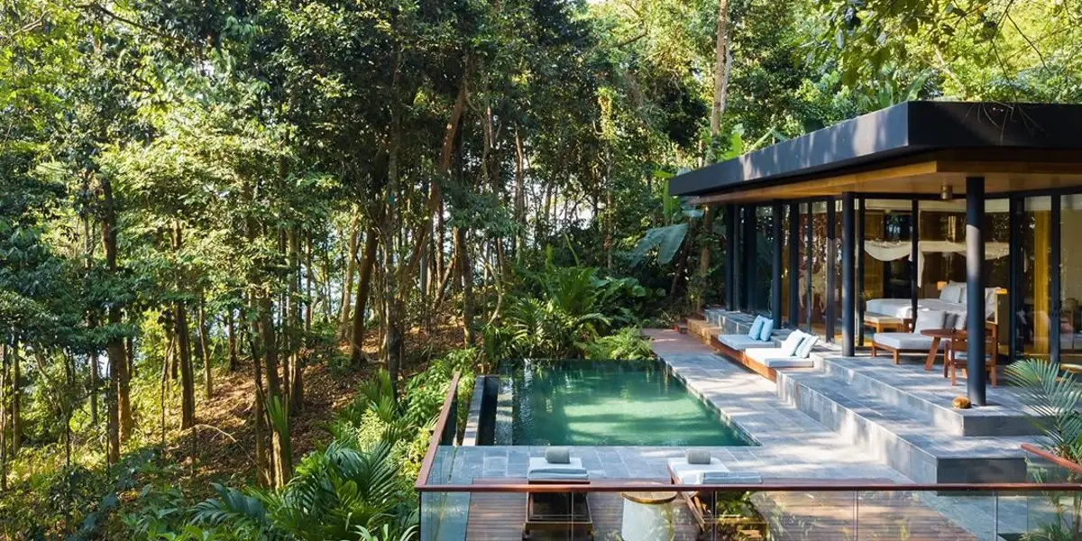 Hotel concierge handing villa keys to guests seated by an infinity pool overlooking the ocean.