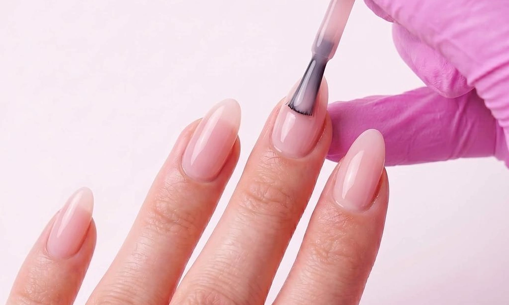 Applying glossy pink gel polish onto freshly cured gel x nails for a polished finish