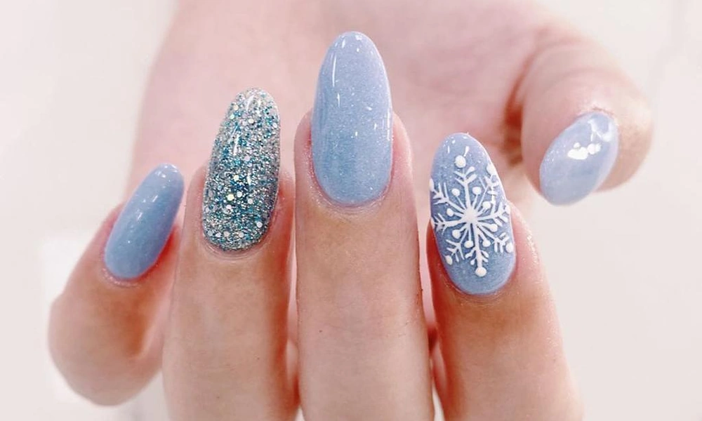 Icy blue Christmas nails adorned with a detailed white snowflake and silver glitter accents