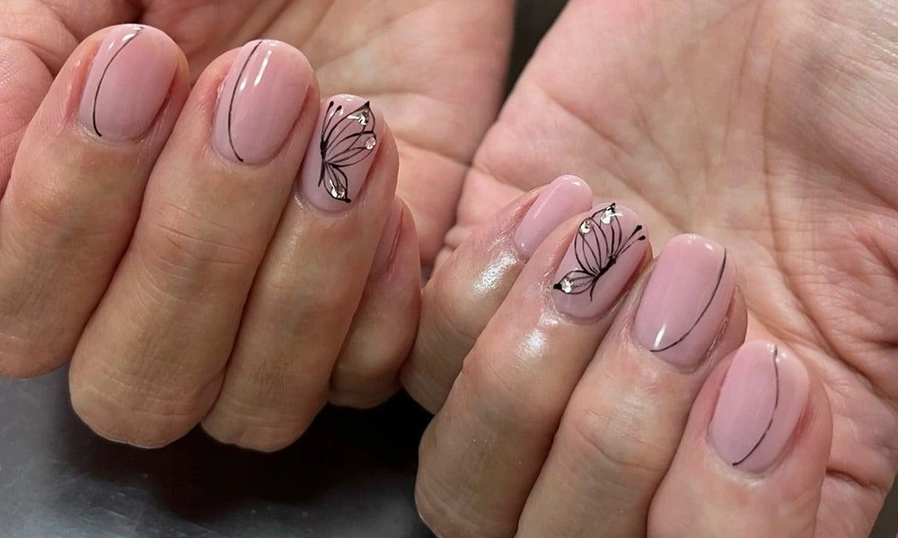 Sheer pink base polish featuring fine black butterfly wing outlines and small rhinestone details