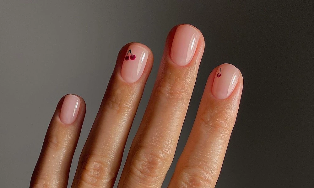 Translucent nude polish accented with miniature hand-painted red cherries on short rounded tips