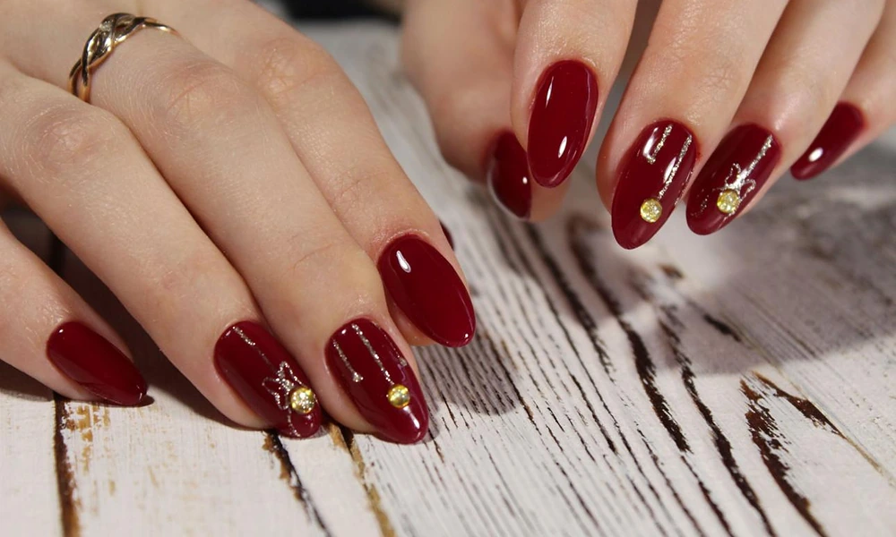 Glamorous burgundy Christmas nails decorated with delicate gold lines and sparkling rhinestones