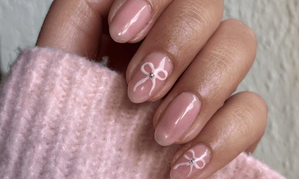 Soft blush pink background detailed with delicate white ribbon bows and tiny rhinestone accents-Cute Nail Ideas