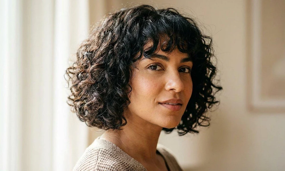 A stylish shoulder-length bob cut featuring soft face-framing curls and bangs