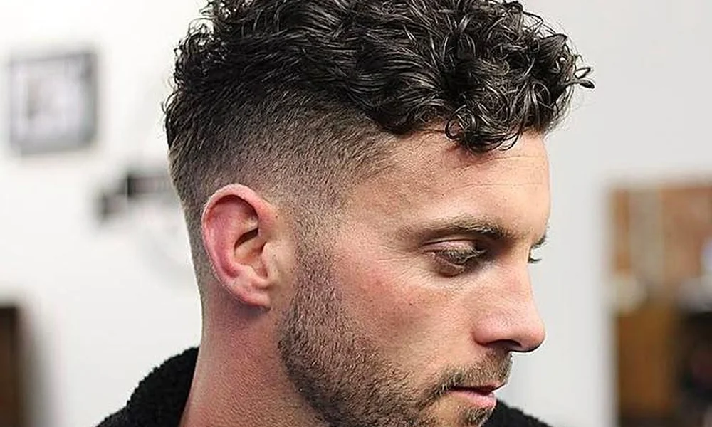 A clean mid-fade haircut paired with short, textured springy coils on top