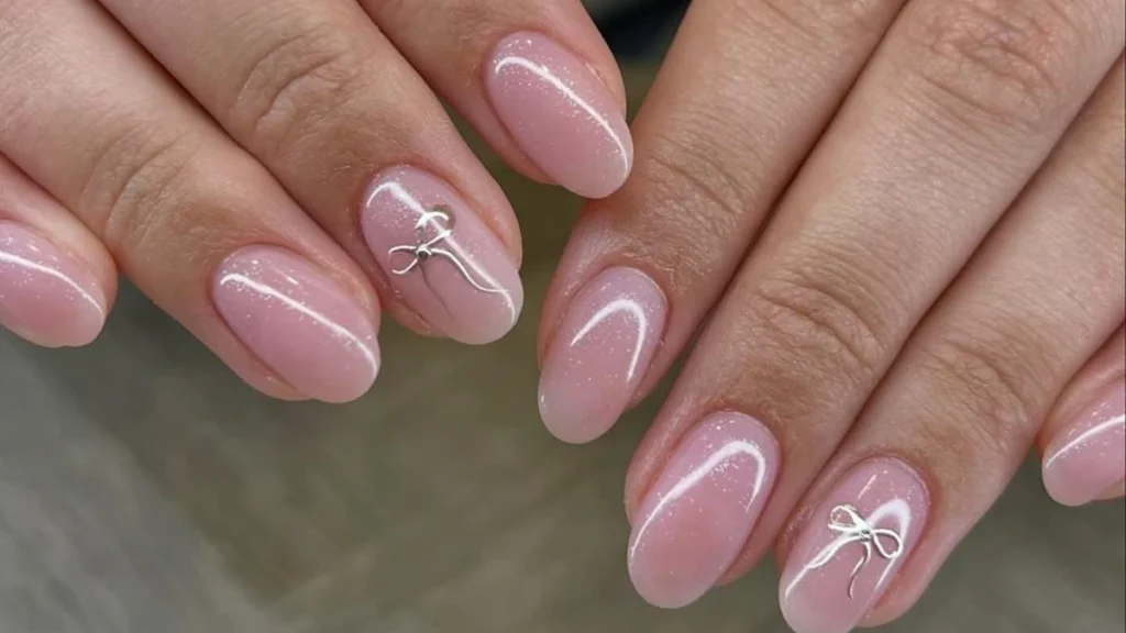 Almond-shaped pink manicure detailed with delicate white bow outlines and subtle shimmer