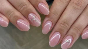 Almond-shaped pink manicure detailed with delicate white bow outlines and subtle shimmer