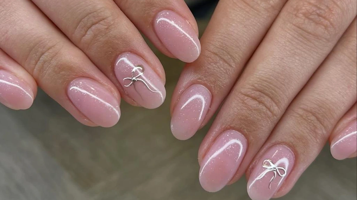 Almond-shaped pink manicure detailed with delicate white bow outlines and subtle shimmer