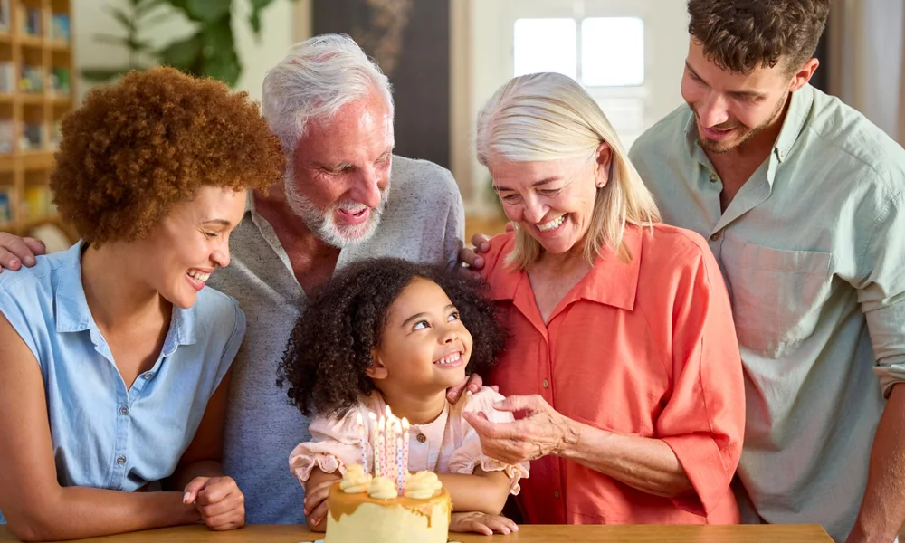 A multi-generational family smiling together around a birthday cake with candles.