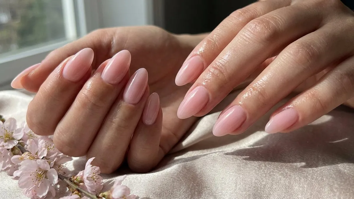Close-up of glossy, natural-looking gel x nails styled in a soft almond shape adorned with flowers