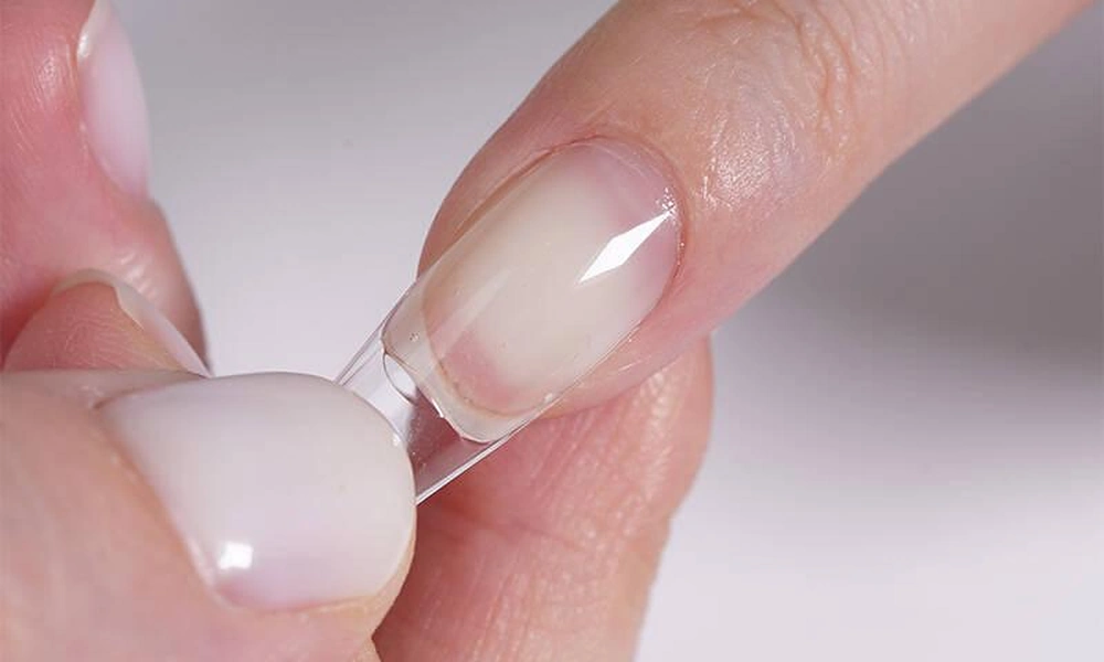 Detailed view of a full-cover soft-gel tip being fitted onto a natural nail for almond gel x nails