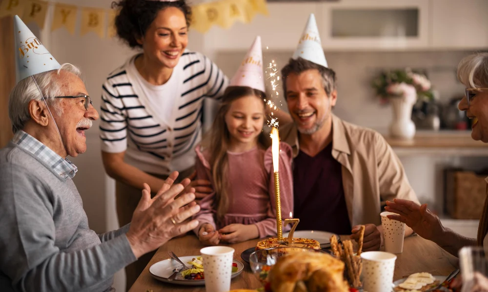 A multi-generational family celebrating a birthday party with cake and party hats at home-Best Dad Jokes and Puns