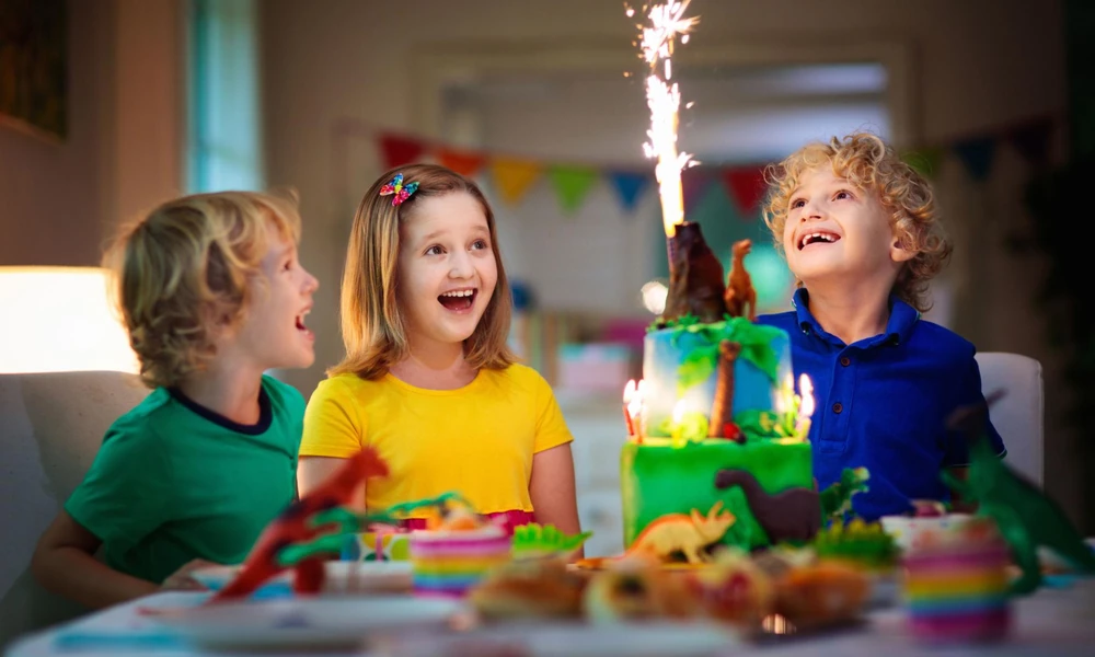 Excited children celebrating a birthday party with a dinosaur-themed cake and sparklers-puns for kids