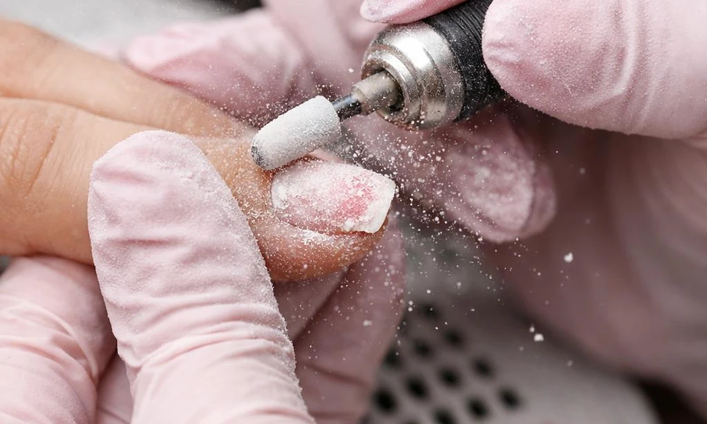 Nail technician using an e-file for professional natural nail prep before gel x nails application