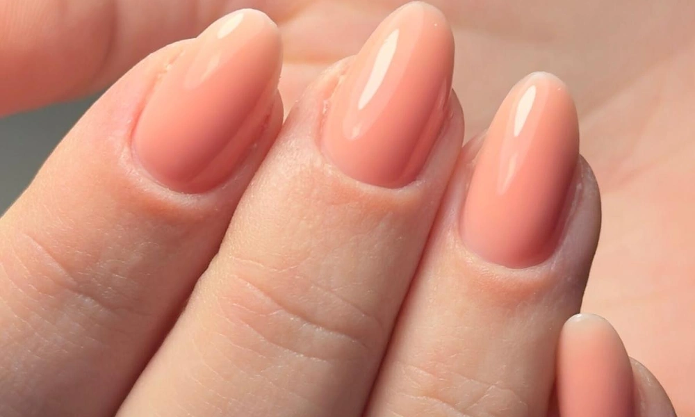 Warm peach-toned glossy gel polish styled smoothly on elegant oval natural nails