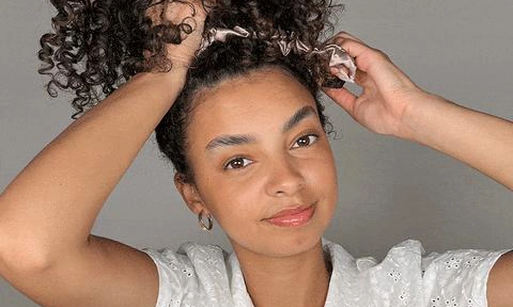 Gathering hair into a loose pineapple topknot using a satin scrunchie to protect texture overnight