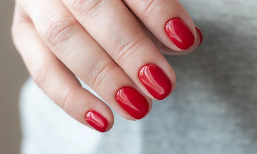 Vibrant cherry red gel polish with a high-shine finish on short rounded square tips