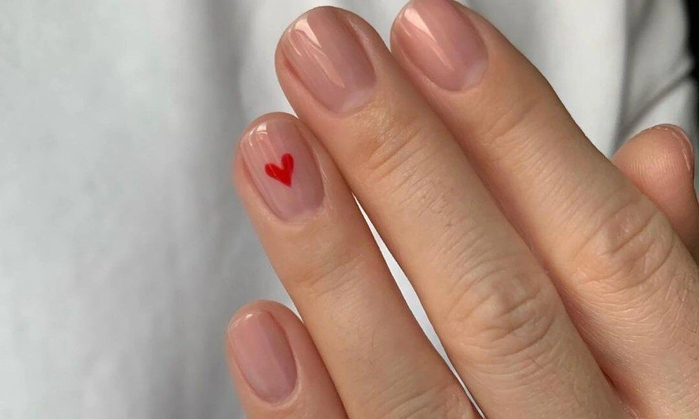Clean short natural nude manicure detailed with a single red micro heart accent-Cute Nail Ideas